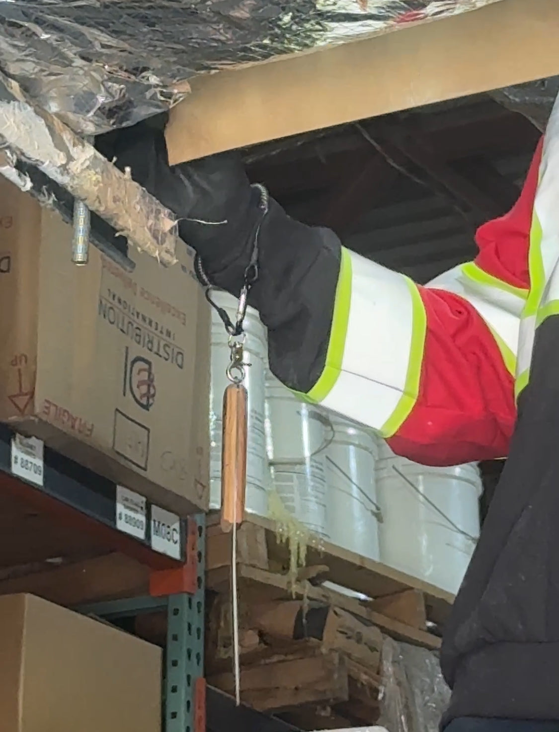 Worker inspecting warehouse ceiling with a long probe, checking for leaks.